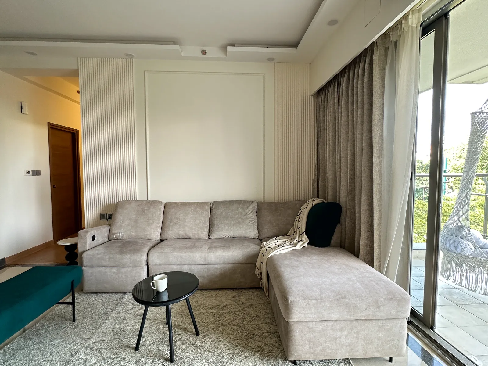 Living room with grey L-shaped sofa and balcony view — Somani's Residence